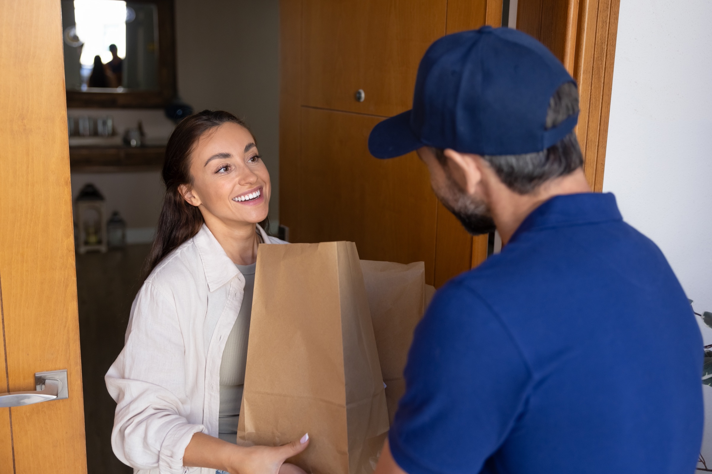 Delivery driver handing a paper bag to a smiling customer at her door